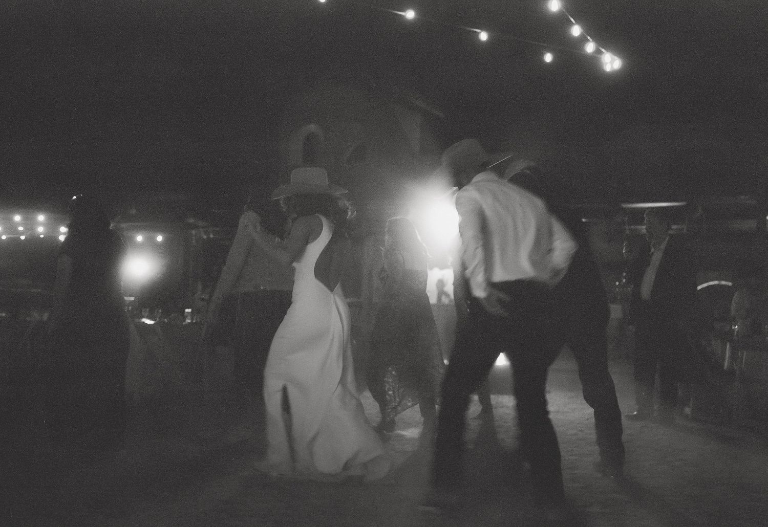 A group of people dancing and enjoying themselves at a nighttime outdoor party with glowing lights in the background.