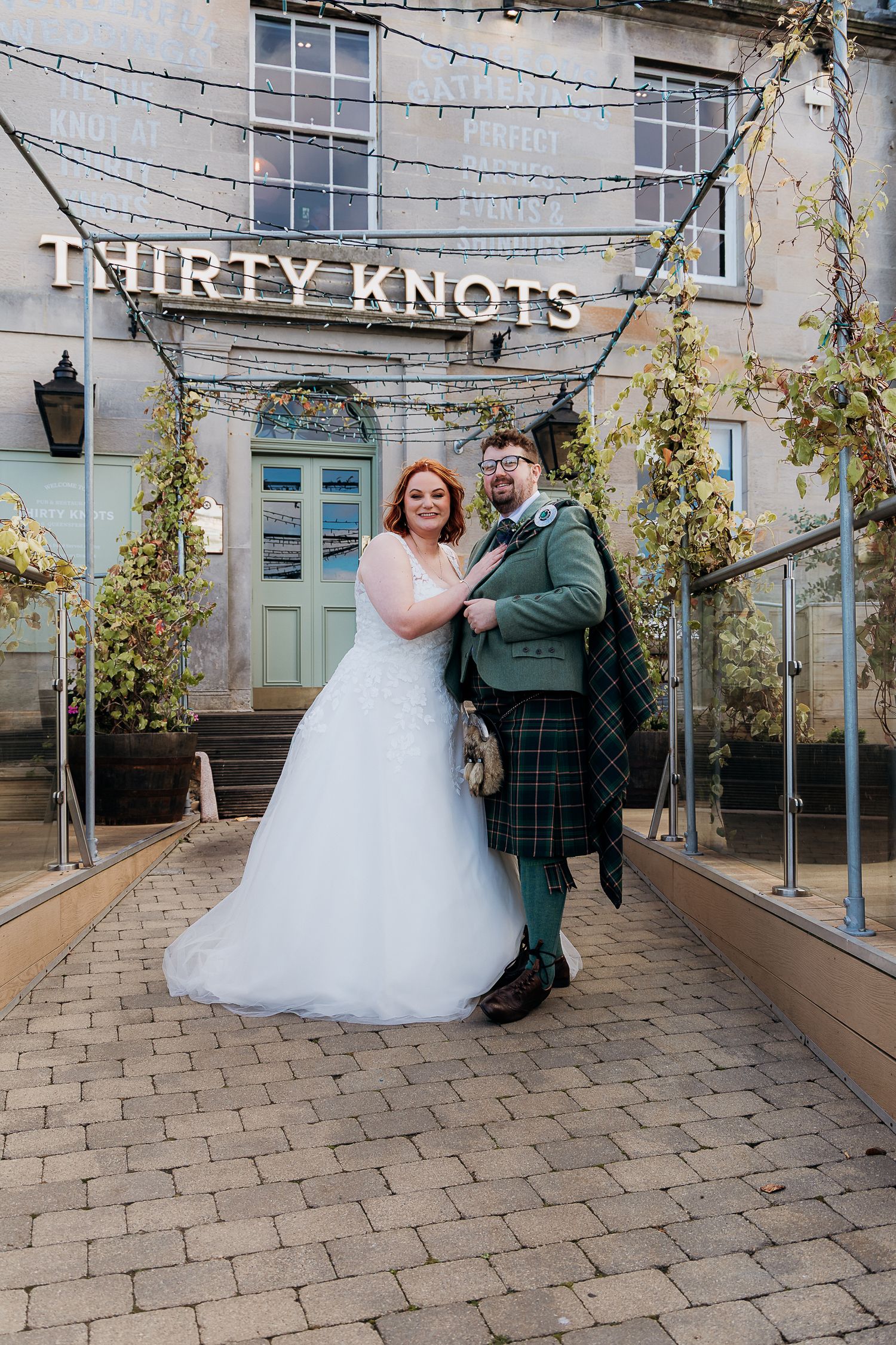 Wedding couple poses outside Thirty Knots venue with groom in traditional Scottish kilt.