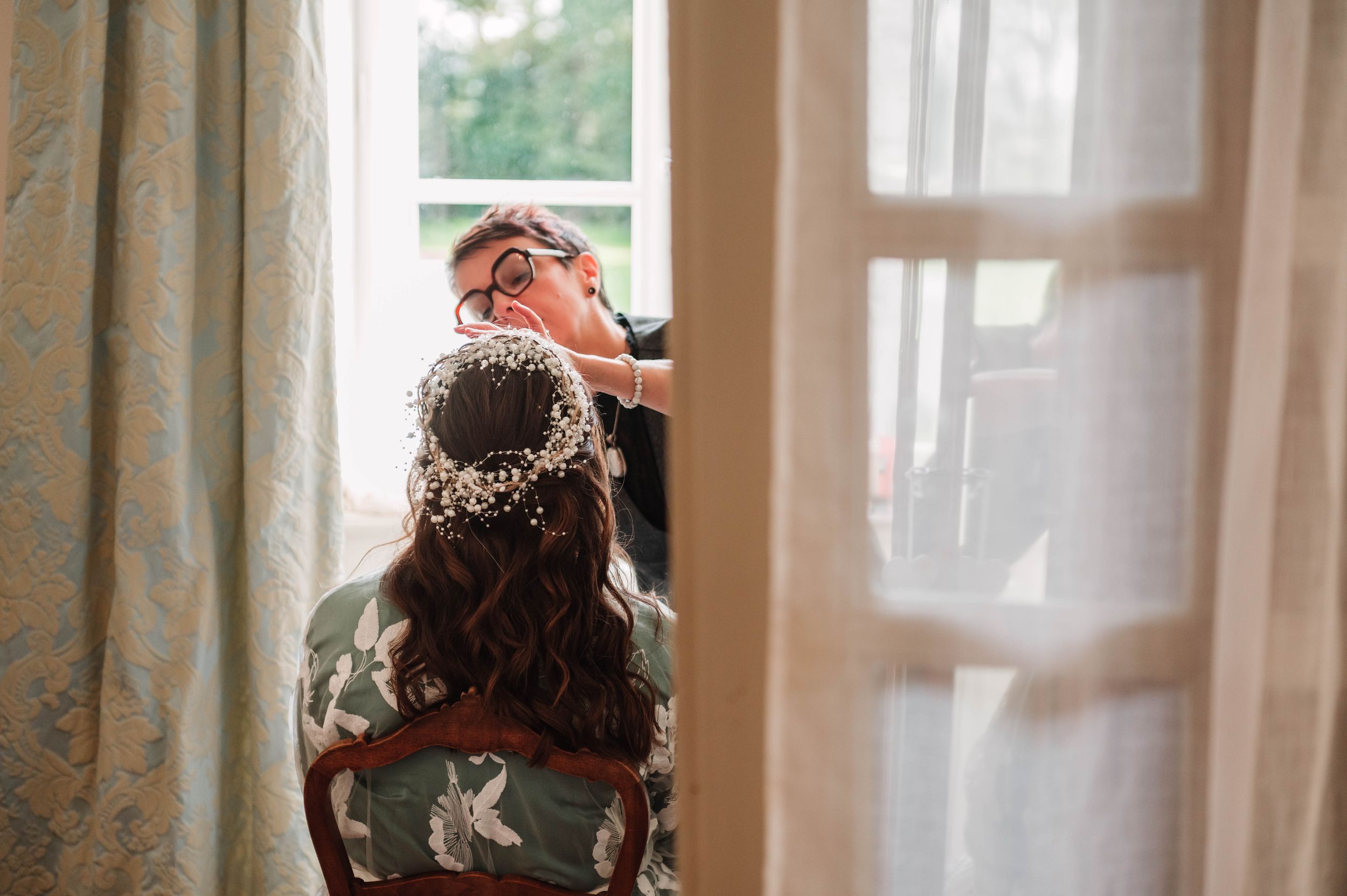 Préparatifs de la mariée près d’une fenêtre en lumière naturelle, reportage de mariage en Bretagne.