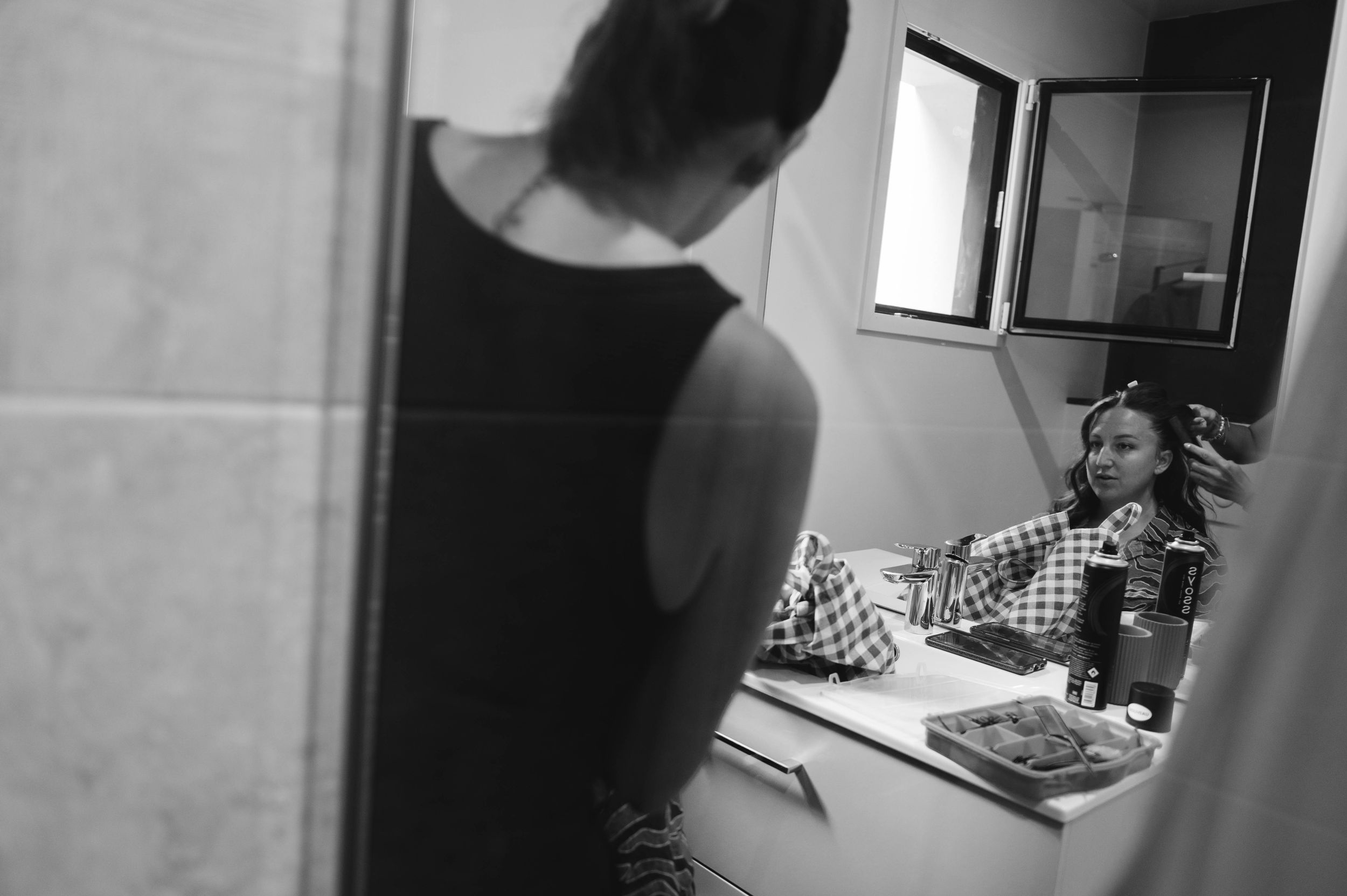 Mariée se préparant devant le miroir lors des préparatifs de mariage, photo en noir et blanc.