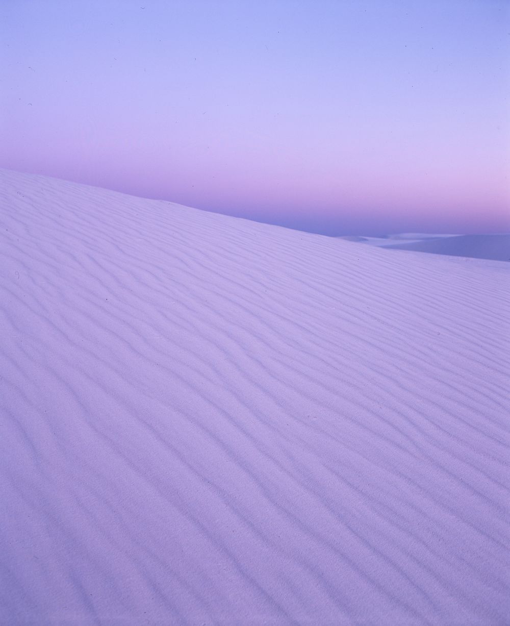 Pink-tinted sand dunes create delicate ripple patterns in soft evening light.