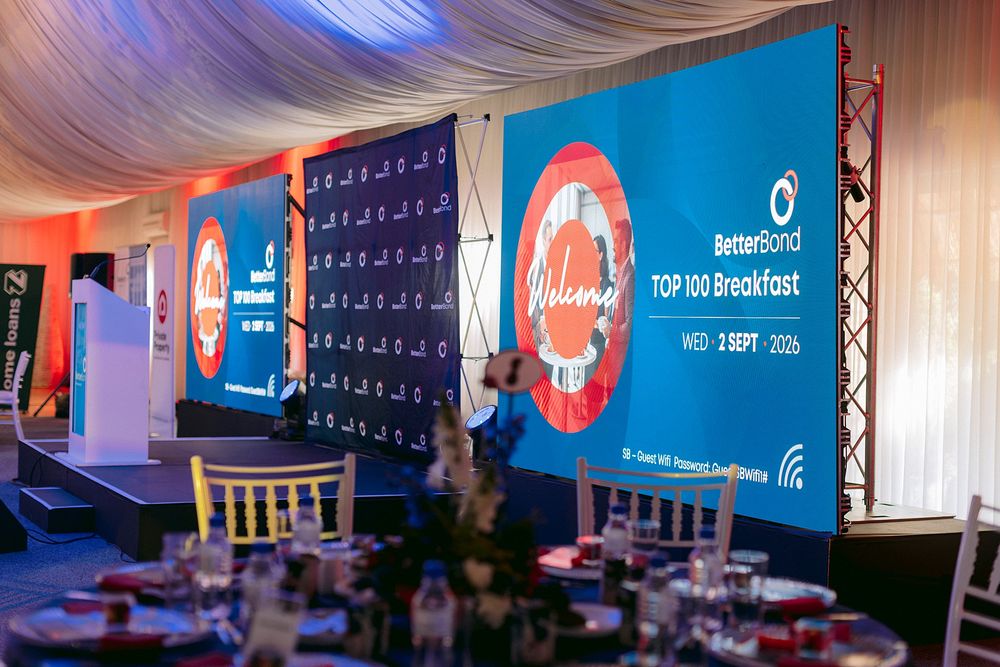 BetterBond Top 100 Breakfast event setup with branded stage backdrop and elegantly set dining tables.