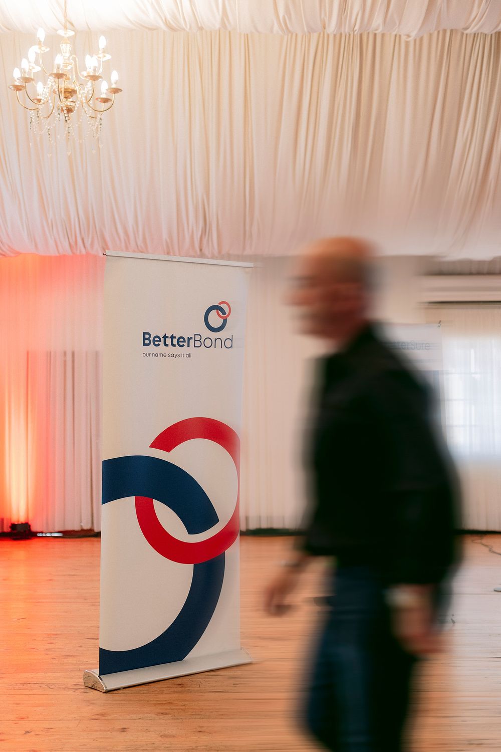 BetterBond branded pull-up banner display at a corporate event with a blurred person walking past.