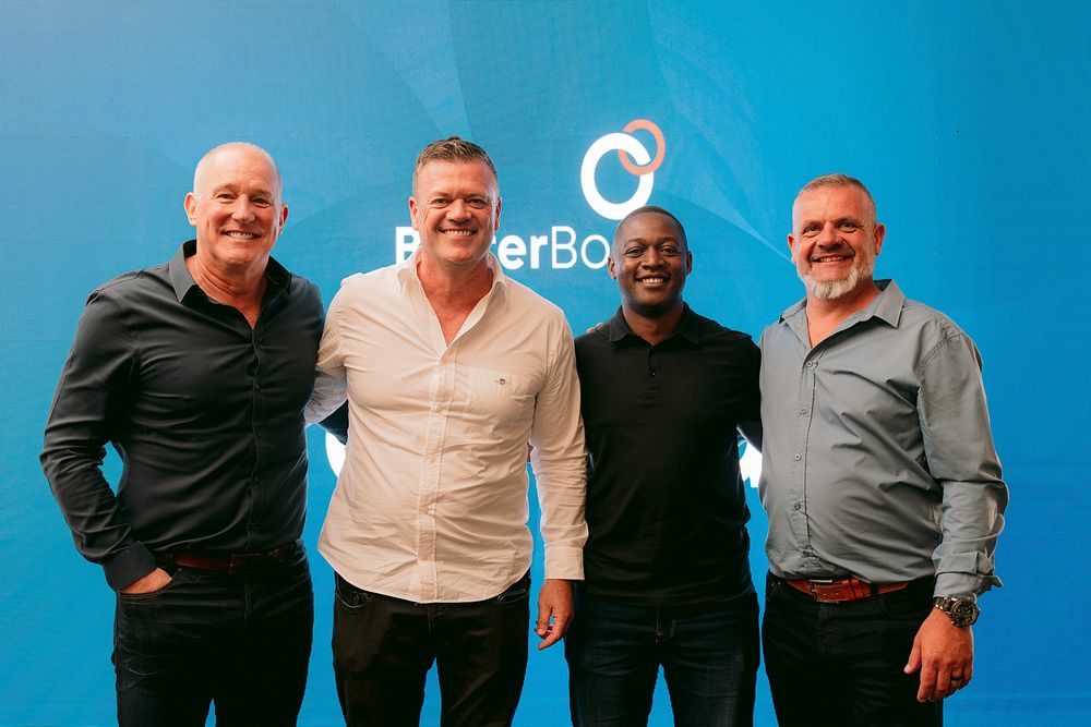 Four men smiling and posing together in front of a blue PokerBros branded backdrop at a corporate event.