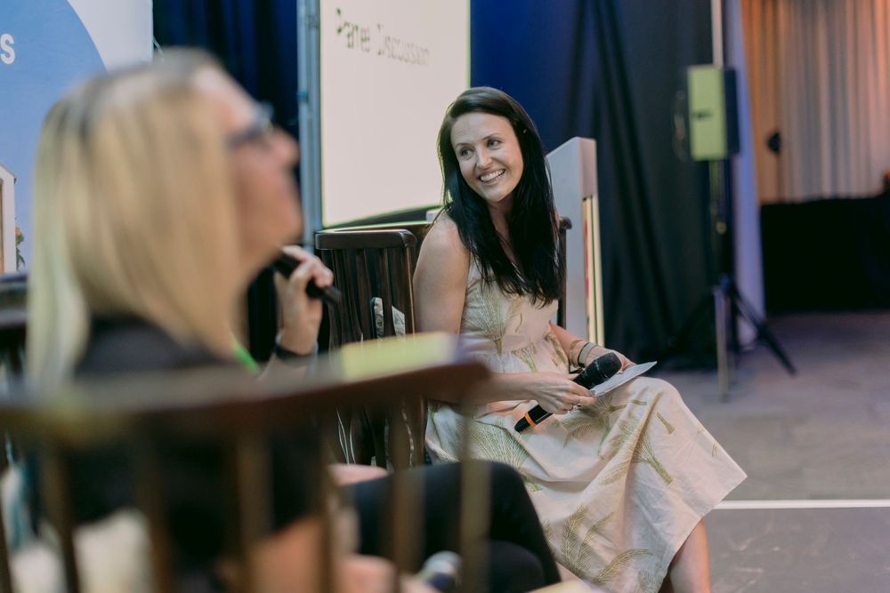Smiling dark-haired woman seated on stage during a panel discussion at a conference event.