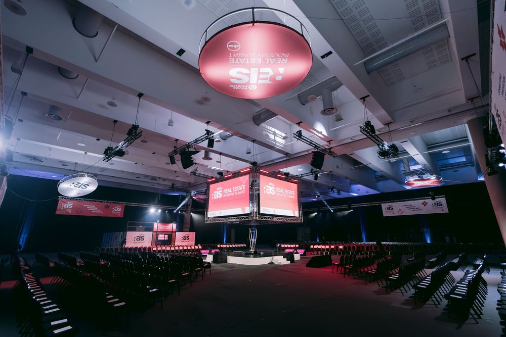 Empty REIS conference hall with large red screens and rows of chairs.