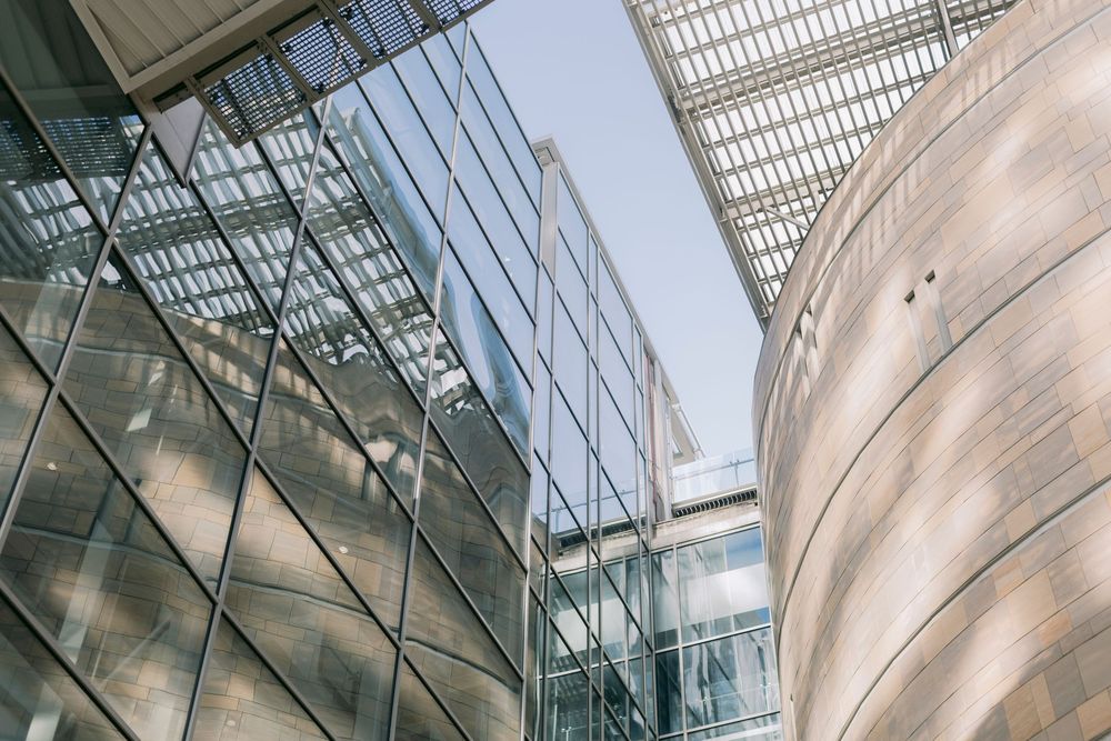 Modern glass and curved concrete building facades photographed from below against a clear blue sky.