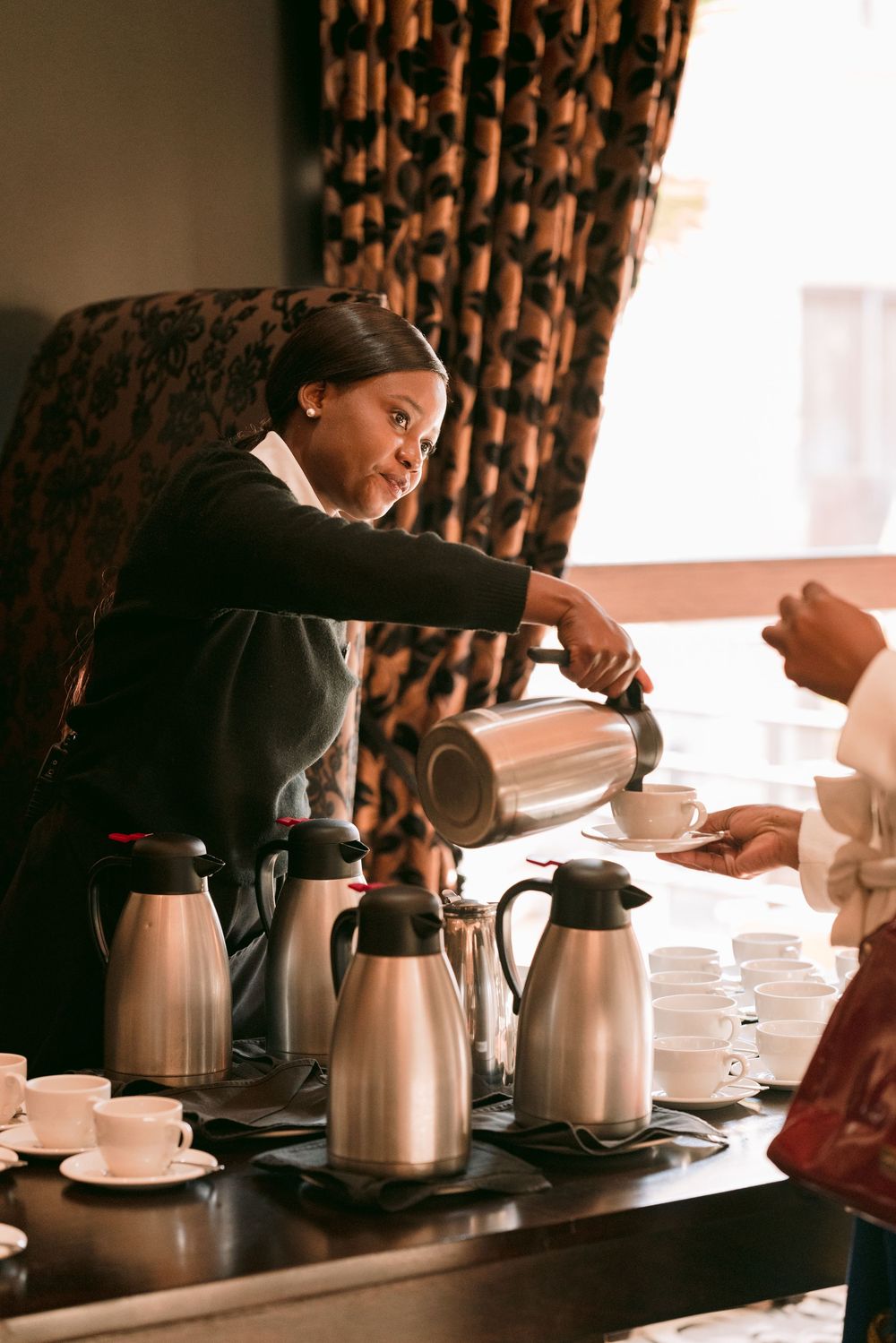 Smiling barista pouring coffee for guest at hospitality service station.