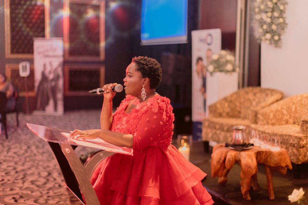 Woman in red ruffled dress performing as MC or speaker at a formal evening event.