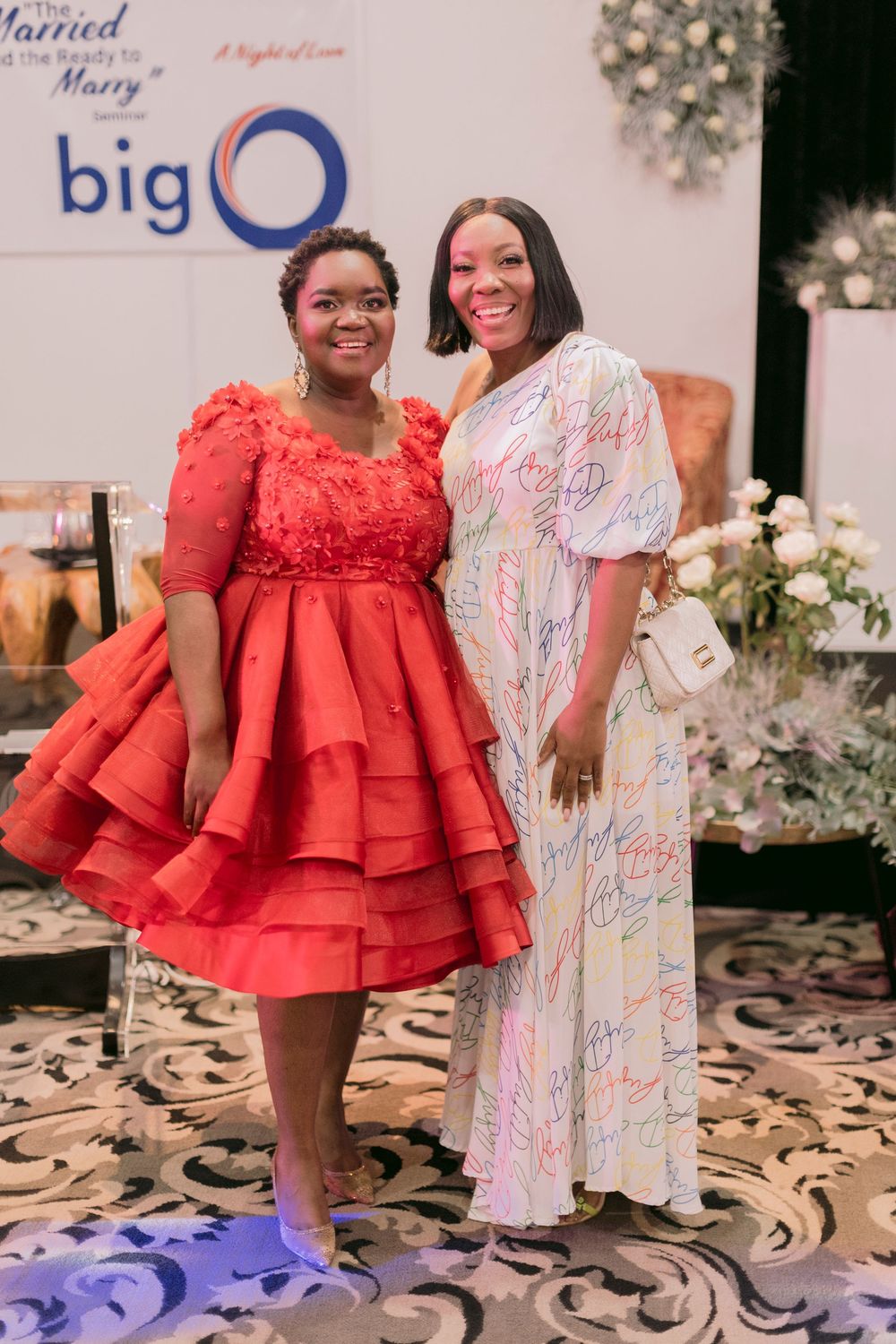 Two women posing together at Big O married event, one in red dress.