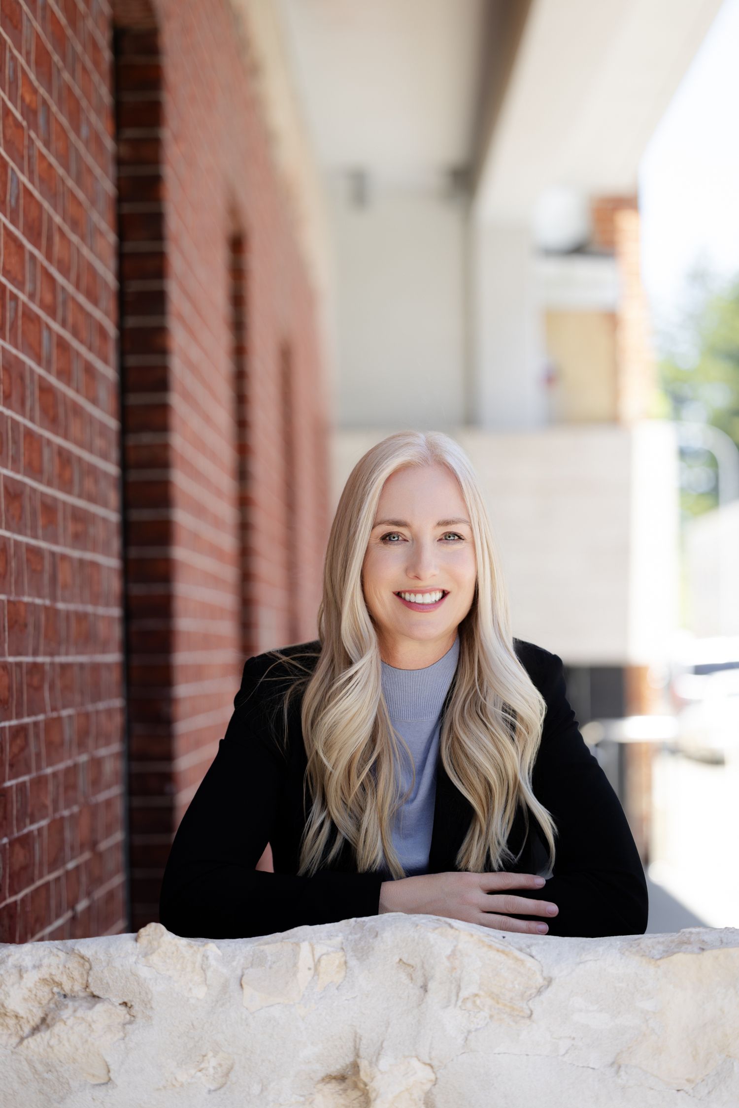 Professional headshot series showing a person in a black blazer and blue top against a brick wall backdrop.