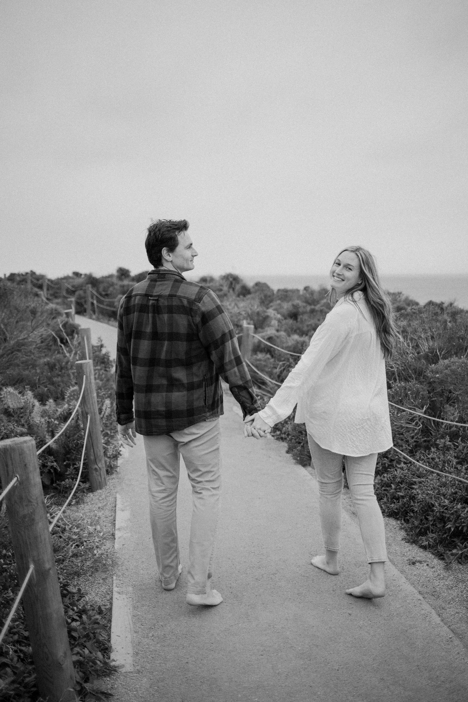 Black and white maternity photo of a couple walking along a coastal path in Malibu