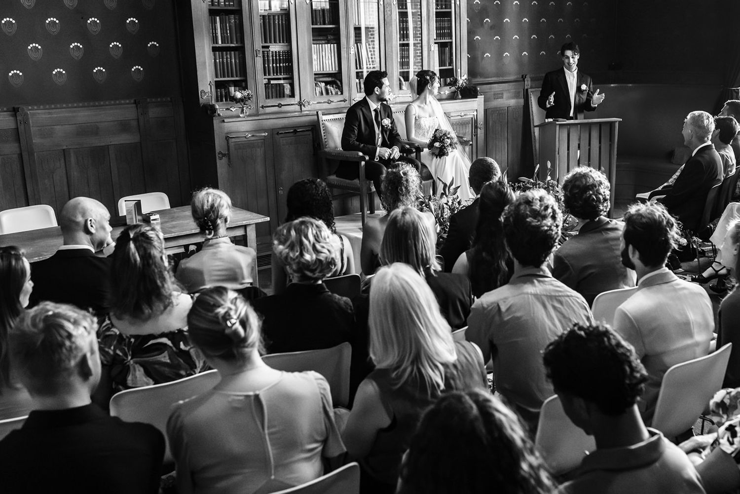Zwart-wit overzichtsfoto van de ceremonie van Sharon en Quinten, met het bruidspaar en de BABS vooraan en gasten van achter gefotografeerd i