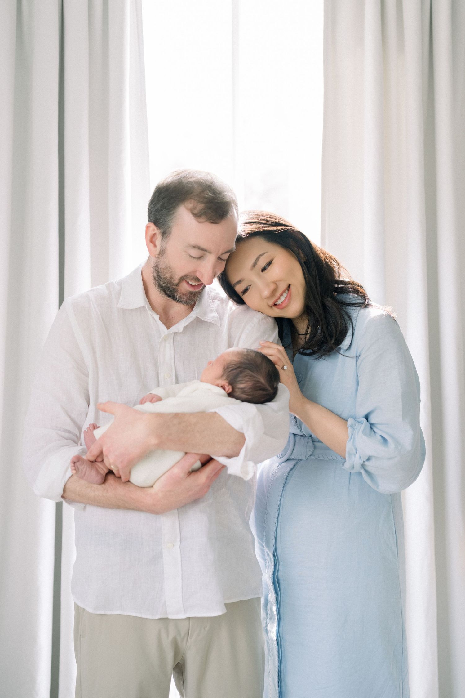 Mother holding newborn near window during an in-home newborn session in Vienna, Virginia