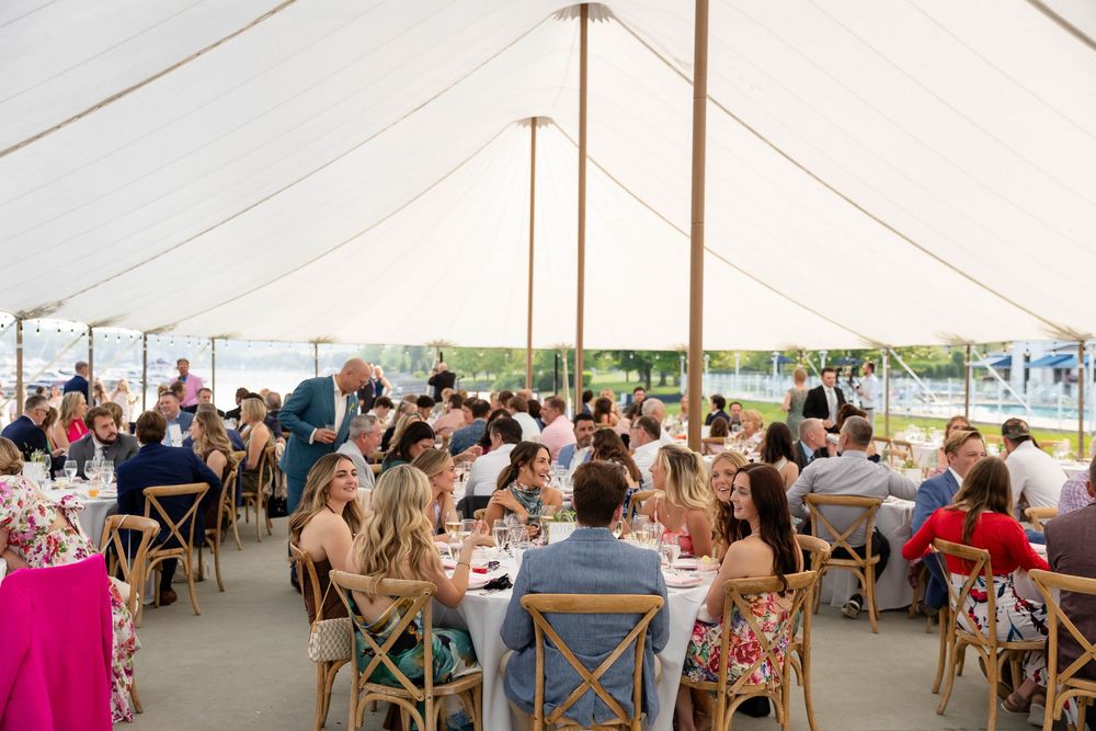 Wedding guests seated at round tables under an elegant white tent for an outdoor reception celebration at Bay Harbor