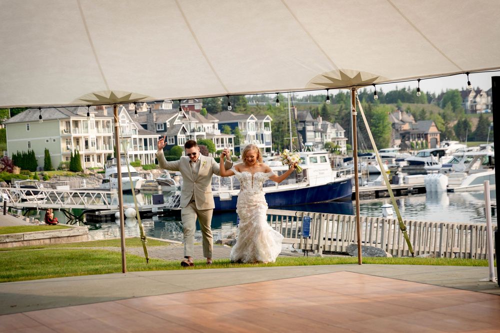 Wedding guests gather at a scenic waterfront venue with boats docked in the marina and white chairs set up for the ceremony.