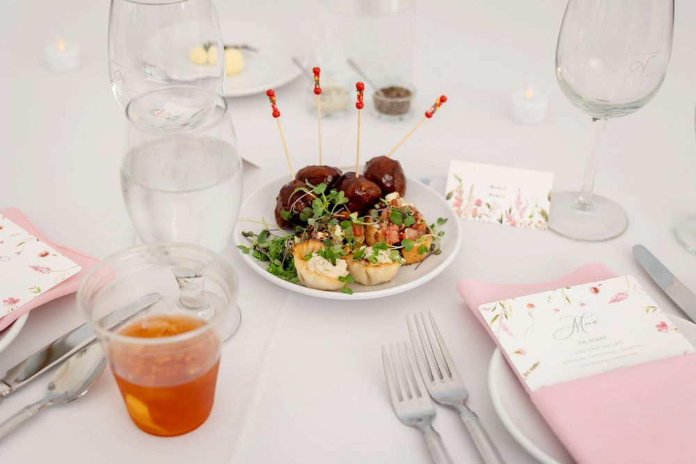 A white dining table setting with pink napkins, glassware, and plates arranged for a formal meal service.