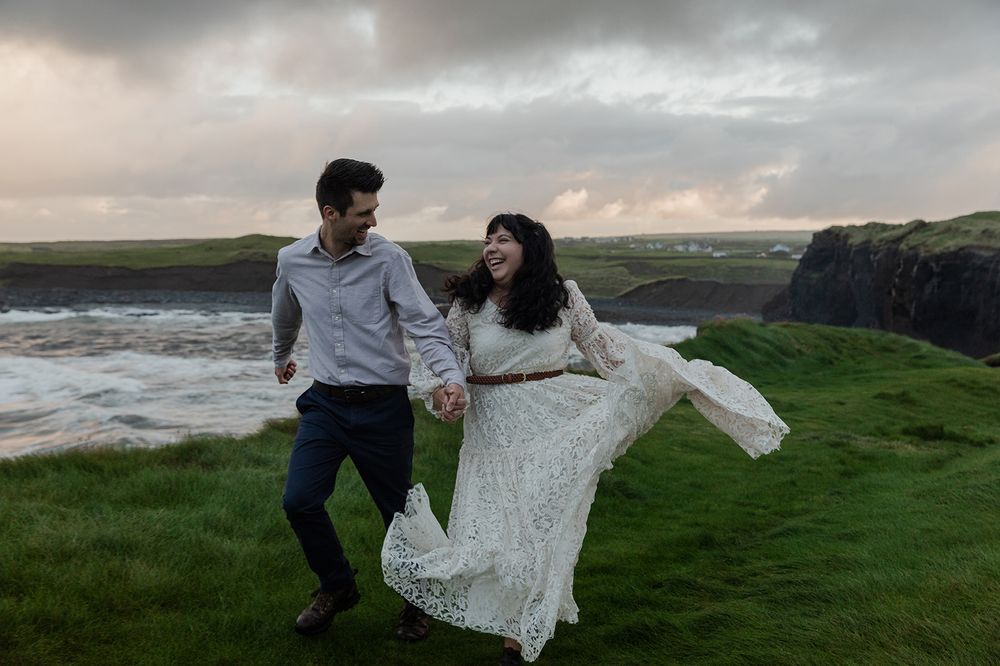 Bride and groom walking along windswept Cliffs of Moher at sunrise