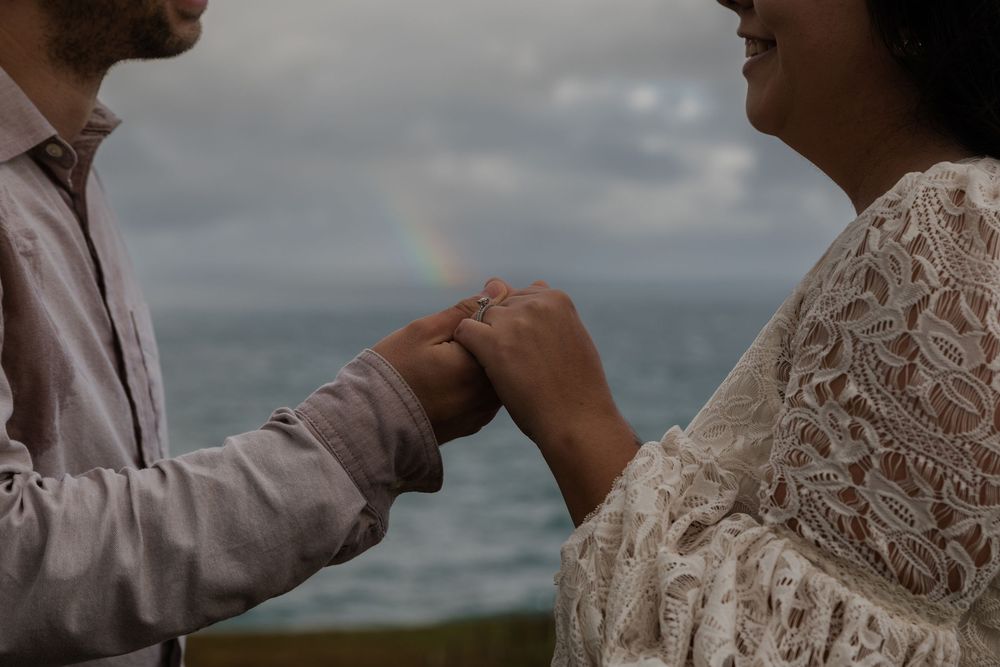 Couple holding hands under the rainbow on Cliffs of Moher during sunrise adventure session