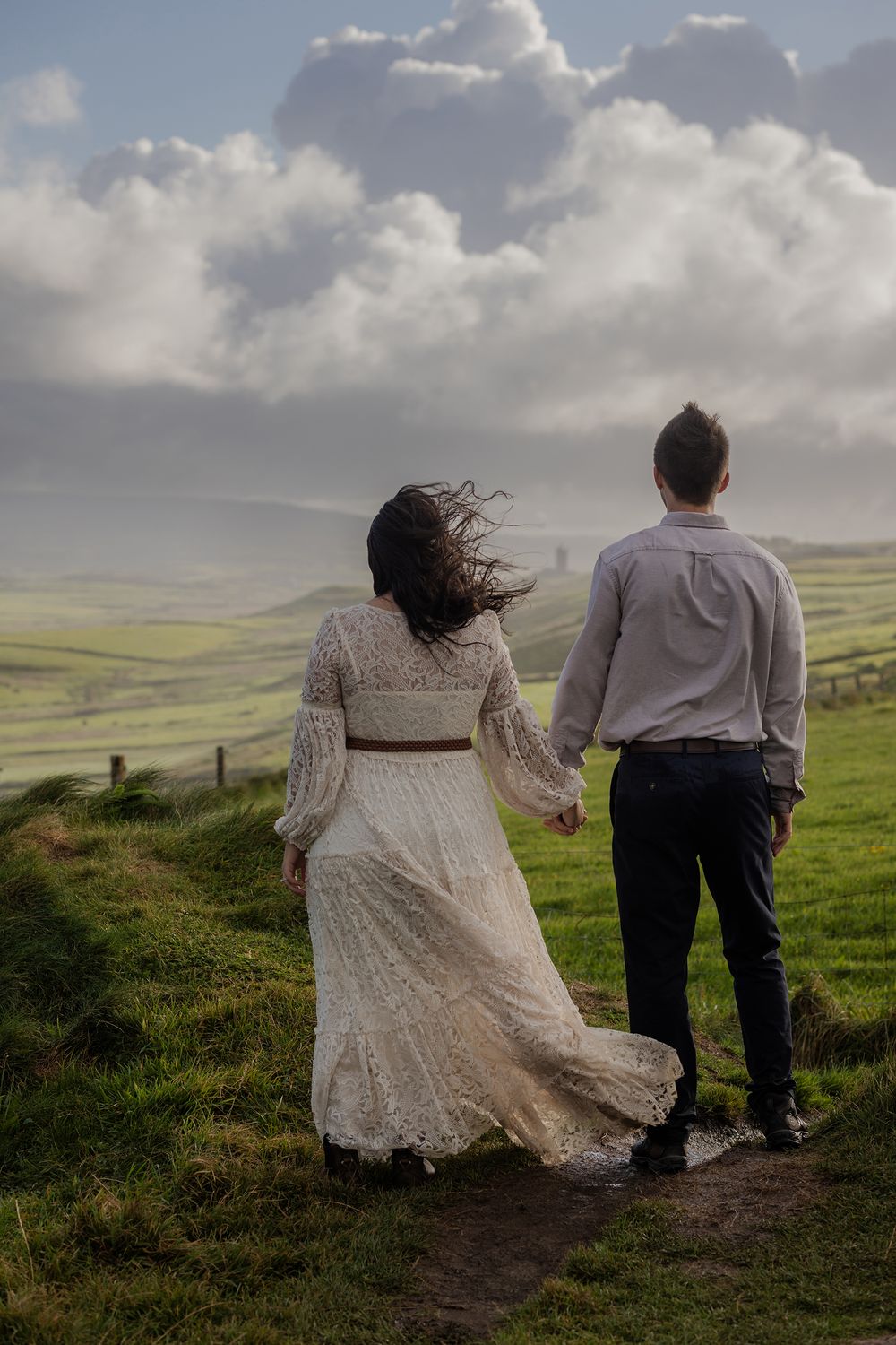 Adventure couple holding hands overlooking Cliffs of Moher at sunrise