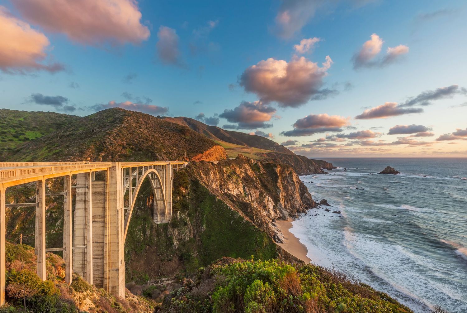 Bixby Creek Bridge along California's Big Sur coastline at sunset with dramatic clouds and rugged cliffs.