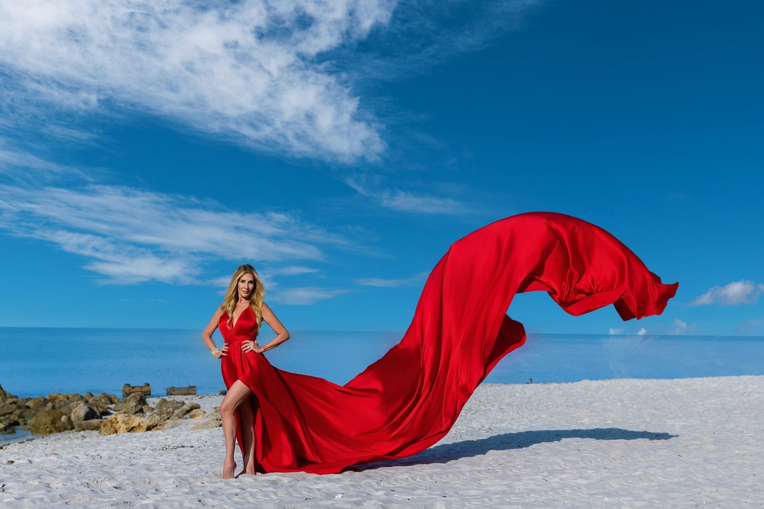 A flowing red dress billows dramatically against a bright blue sky and snowy white landscape.