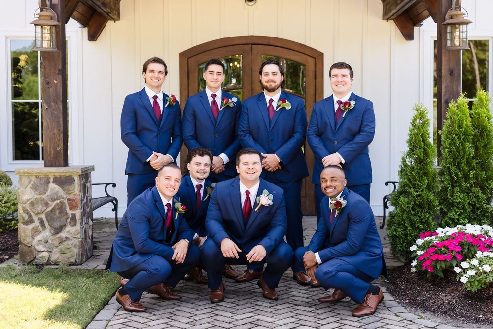 Groomsmen in navy blue suits pose together for a formal wedding photo on stone steps.