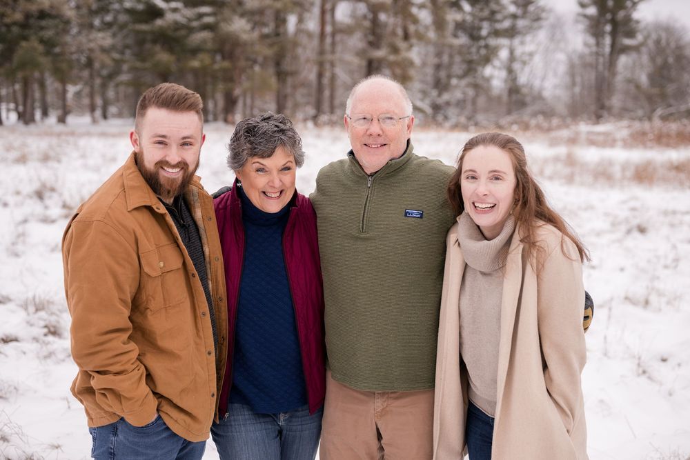 Family group photo in winter setting with snow covered ground and pine trees.