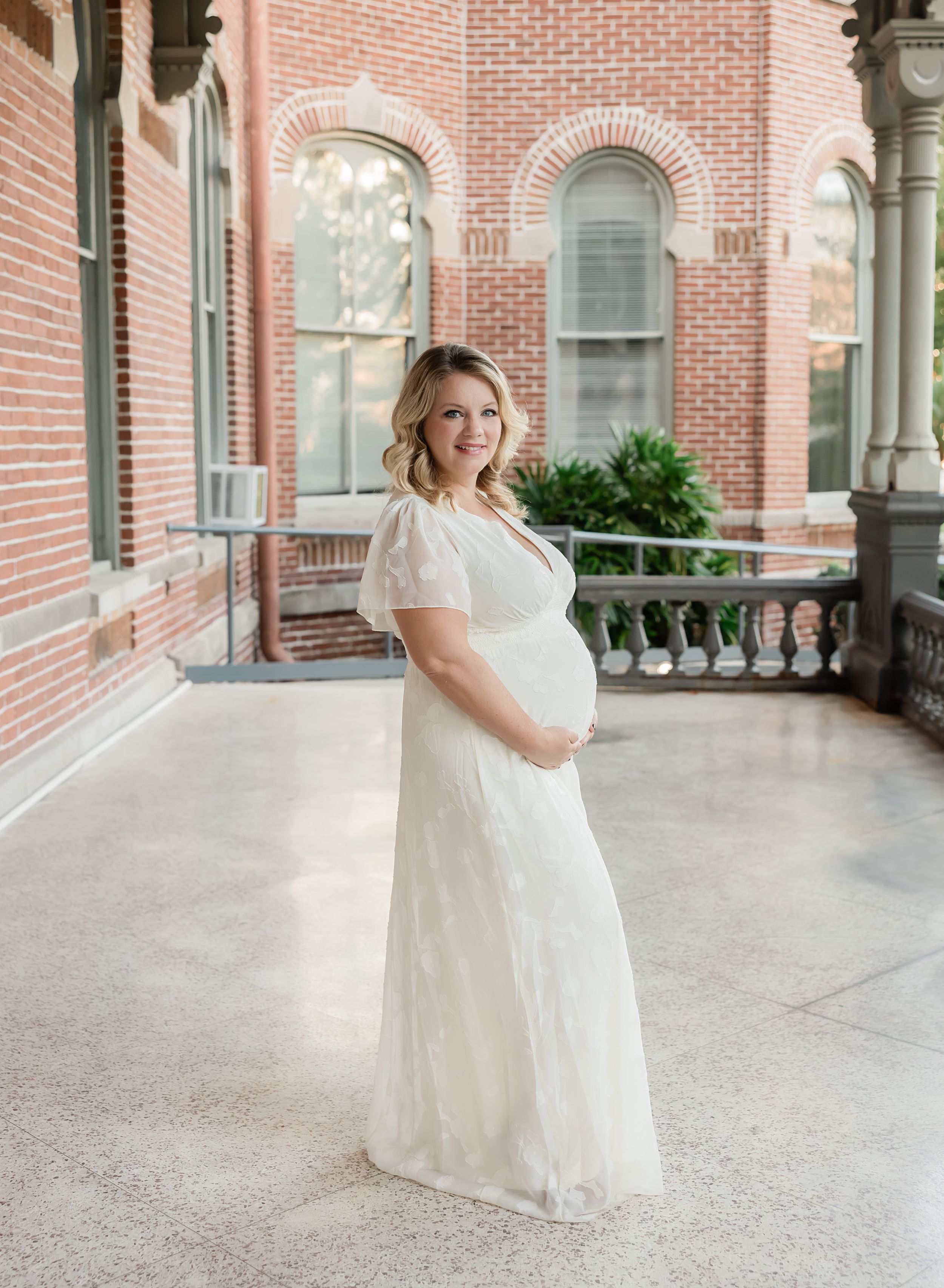 A bride in a flowing white dress twirls gracefully on a columned brick porch at a historic building.