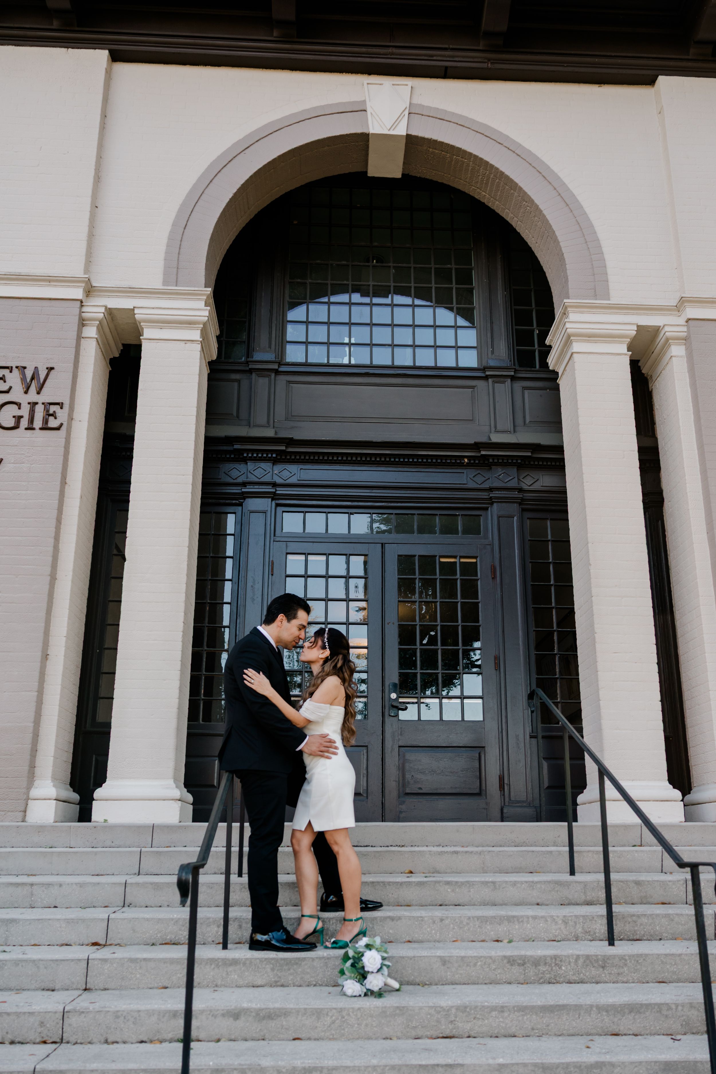 A romantic wedding couple poses next to a vintage white car at sunset.