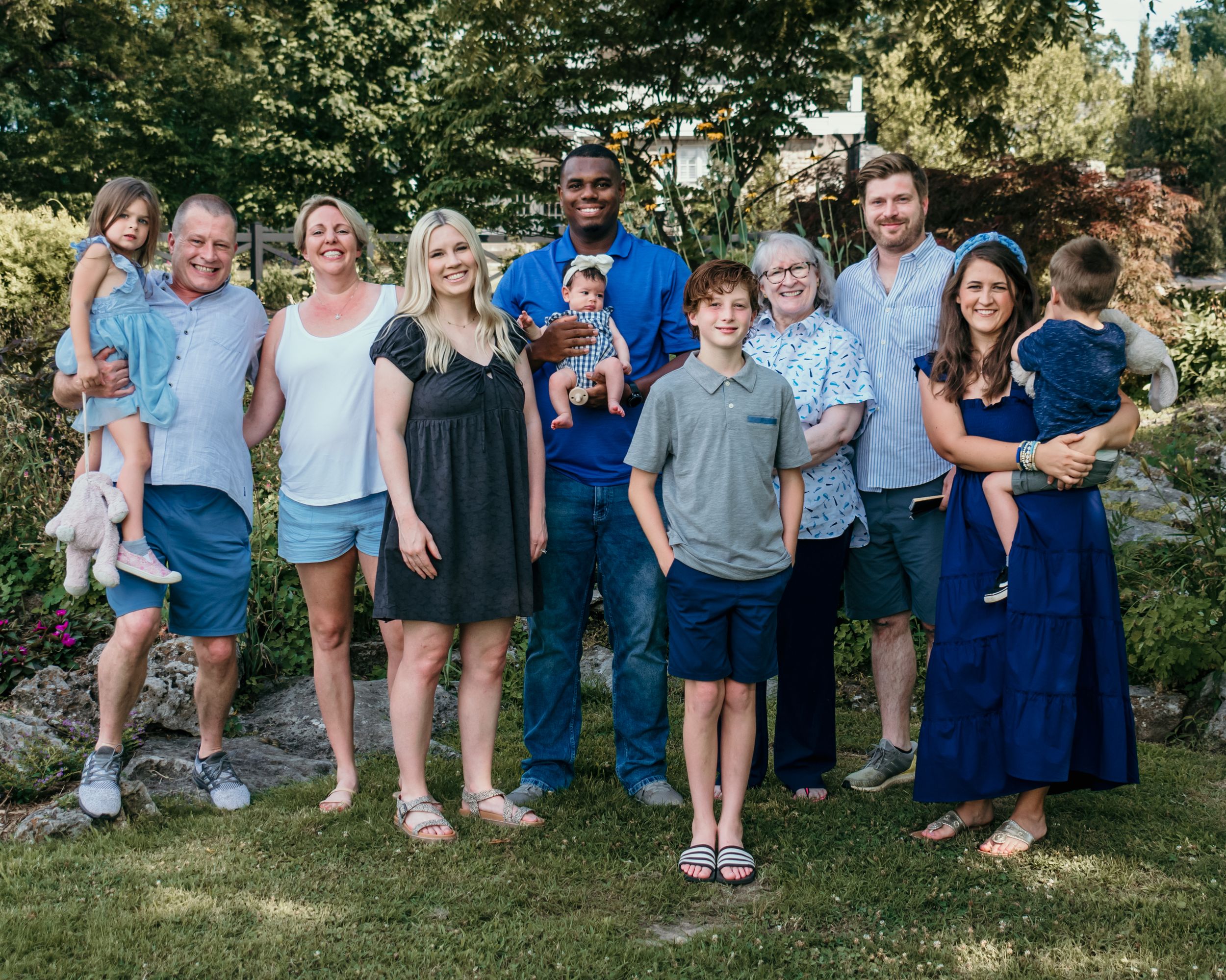 A large family all clad in blue gather outdoors for a casual garden family photo shoot.