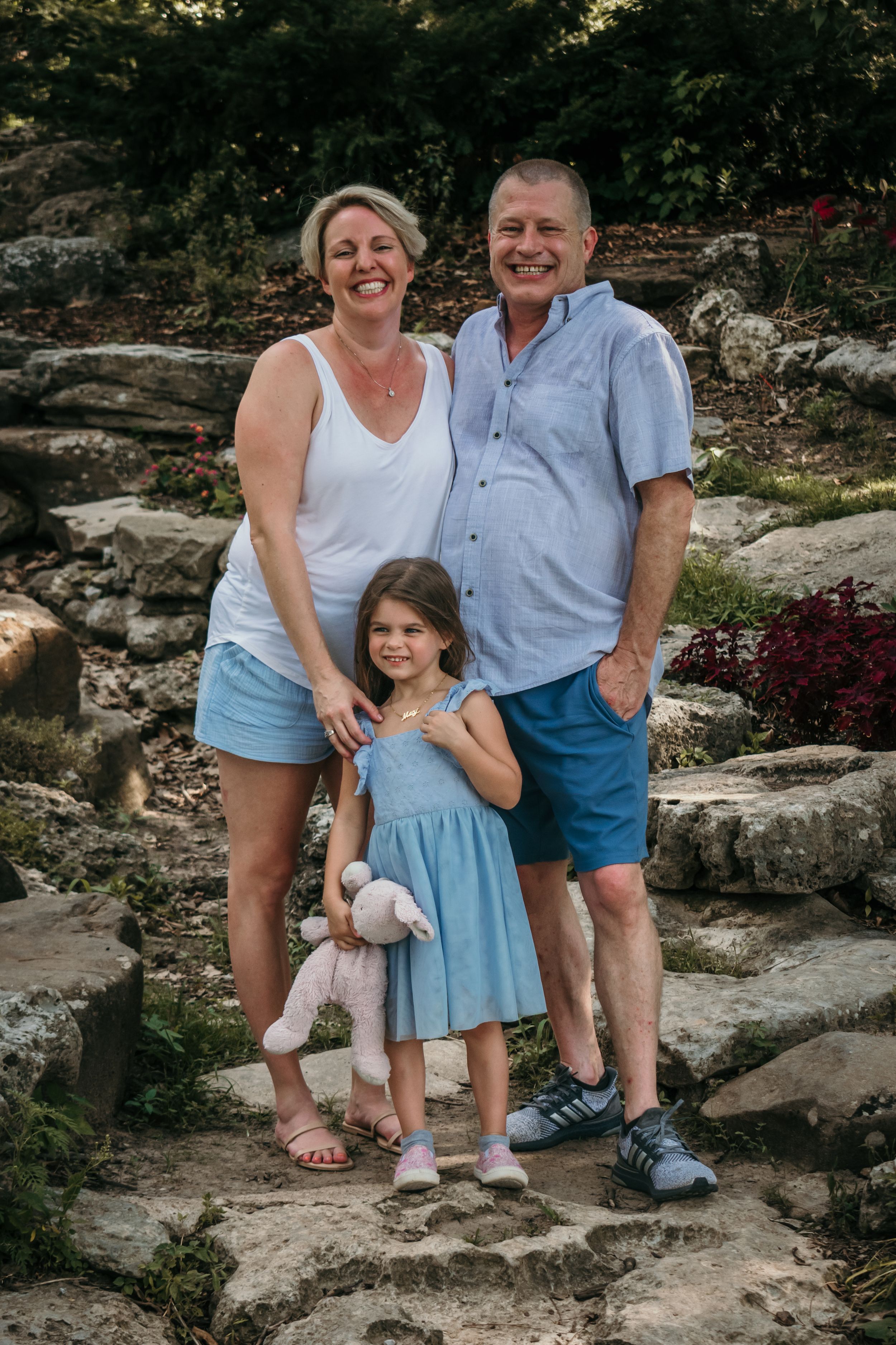 Family portrait session on rocky terrain in matching blue and white outfits at sunset.