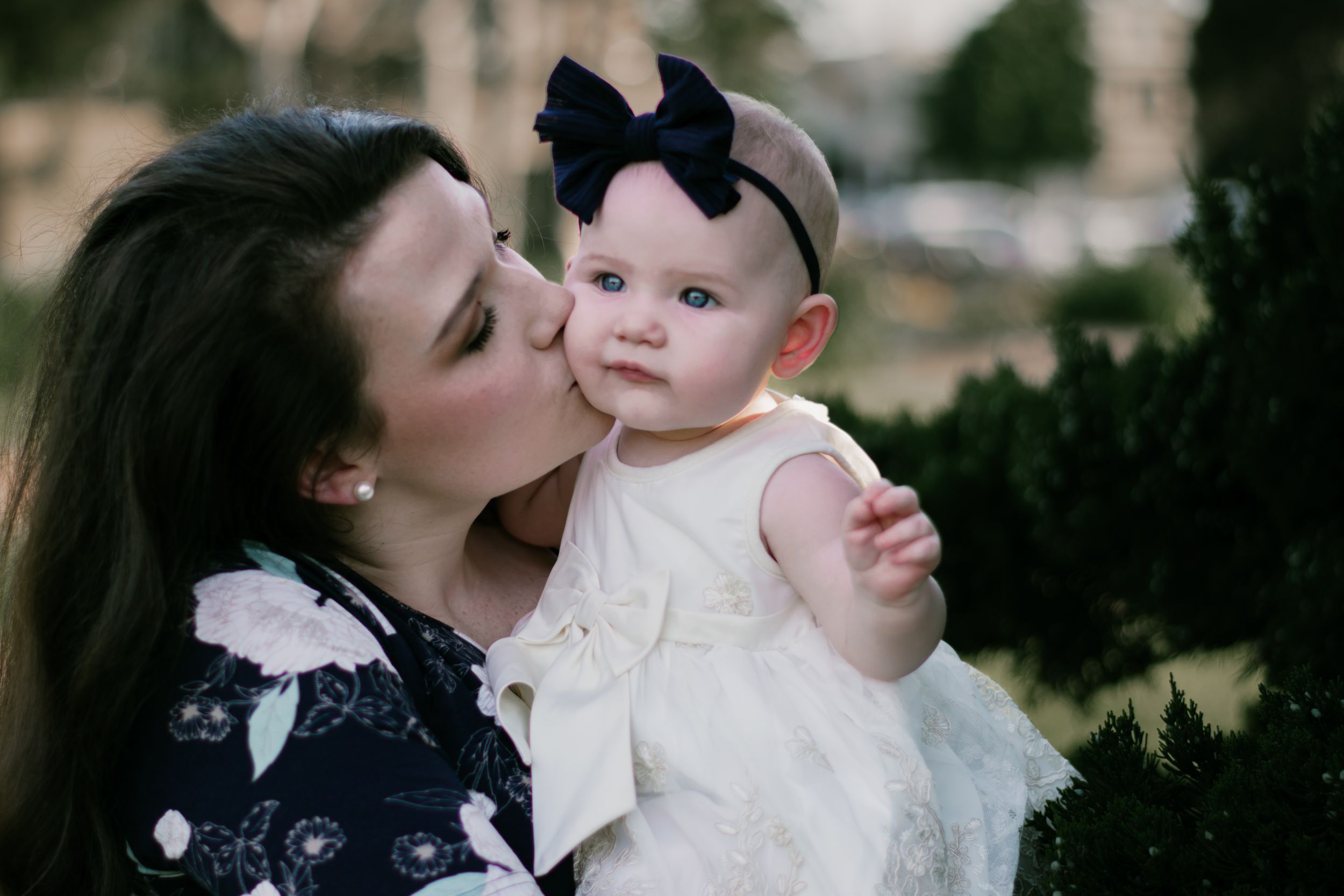 A tender moment between a parent and baby in formal white attire during a portrait session.