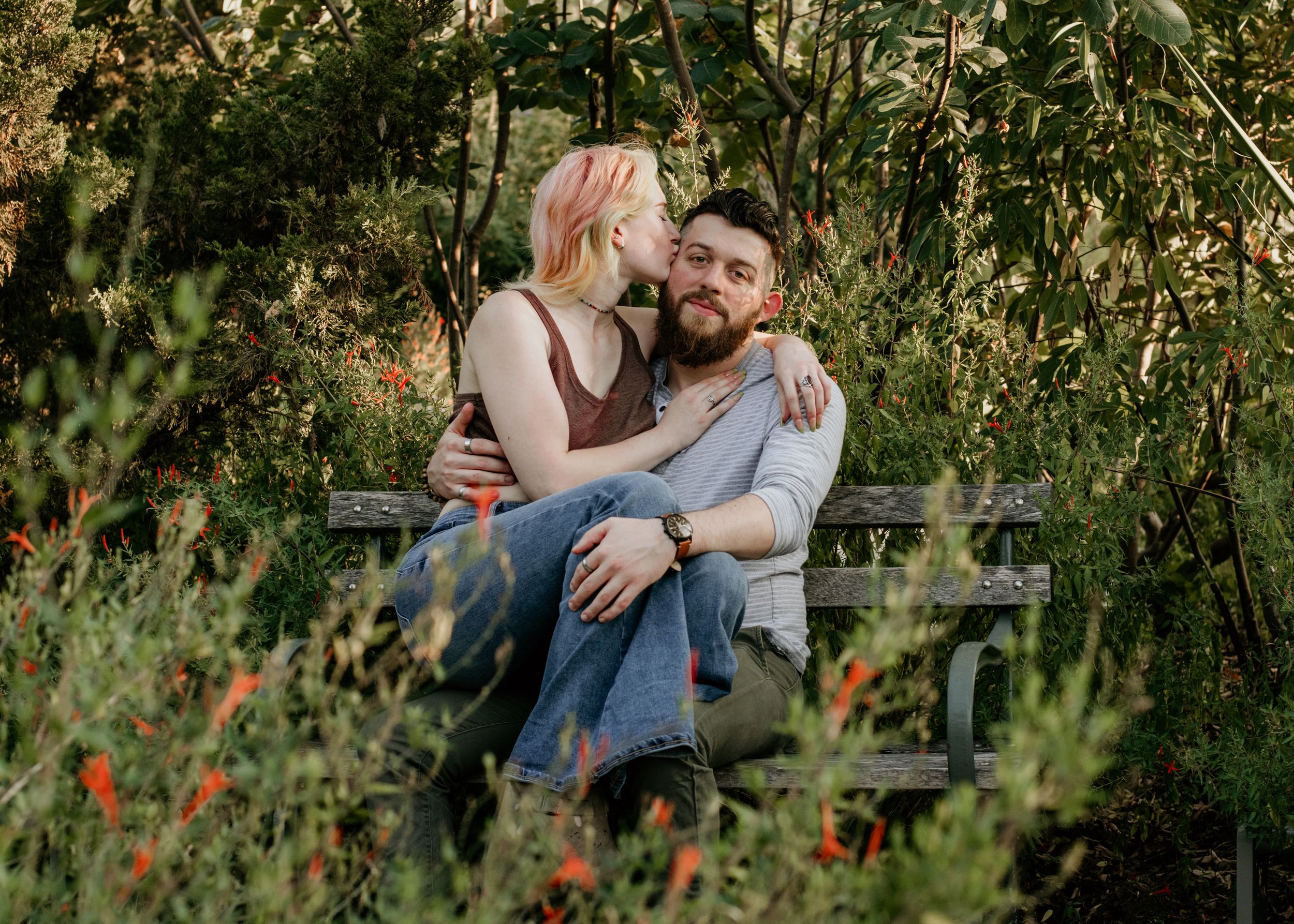 A couple poses cutely, surrounded by a lush garden.
