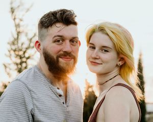 A romantic couple embraces outdoors during golden hour sunset in a candid portrait.