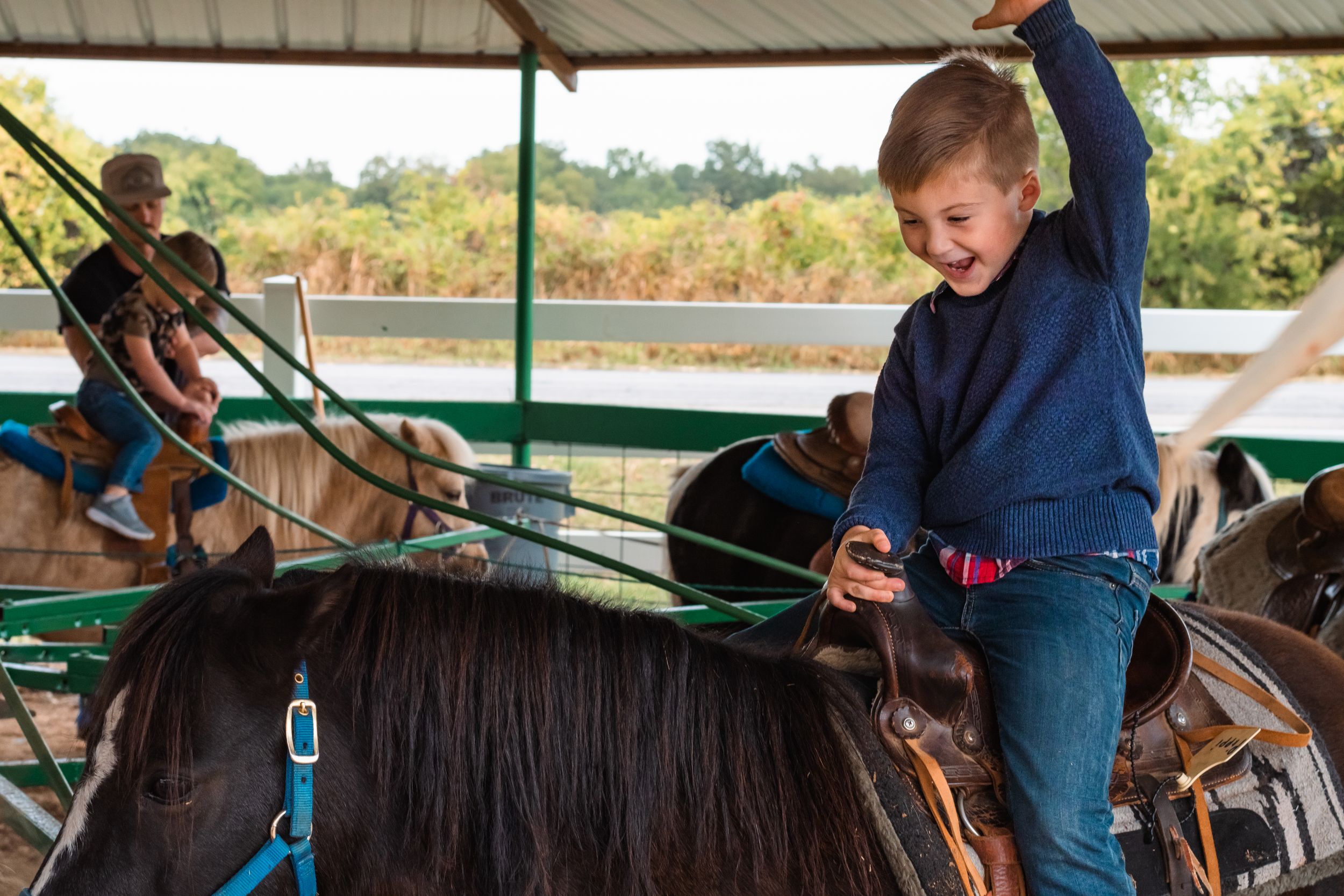 A boy acts out his cowboy fantasy while riding a brown horse at the fair.