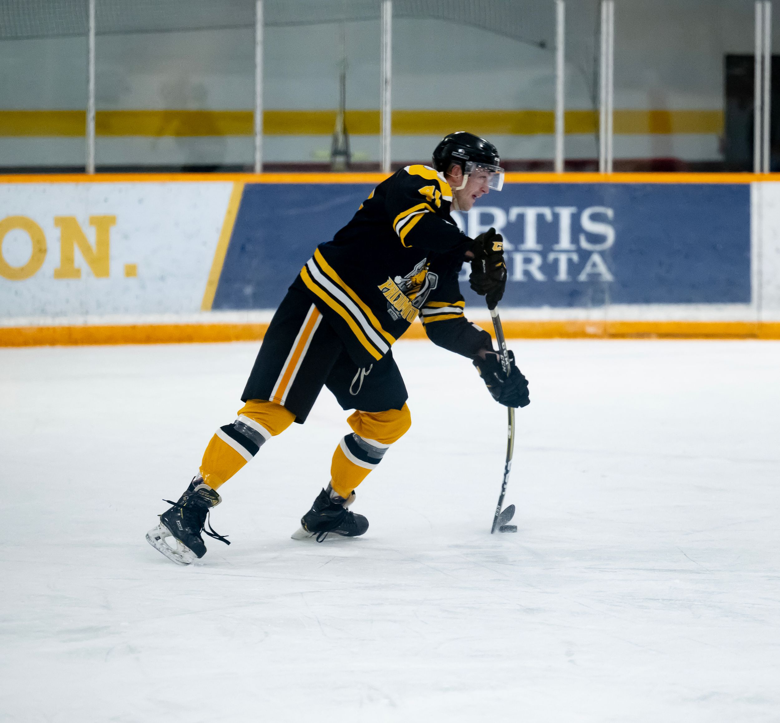 Hockey player in black and yellow uniform skating on ice during practice session.