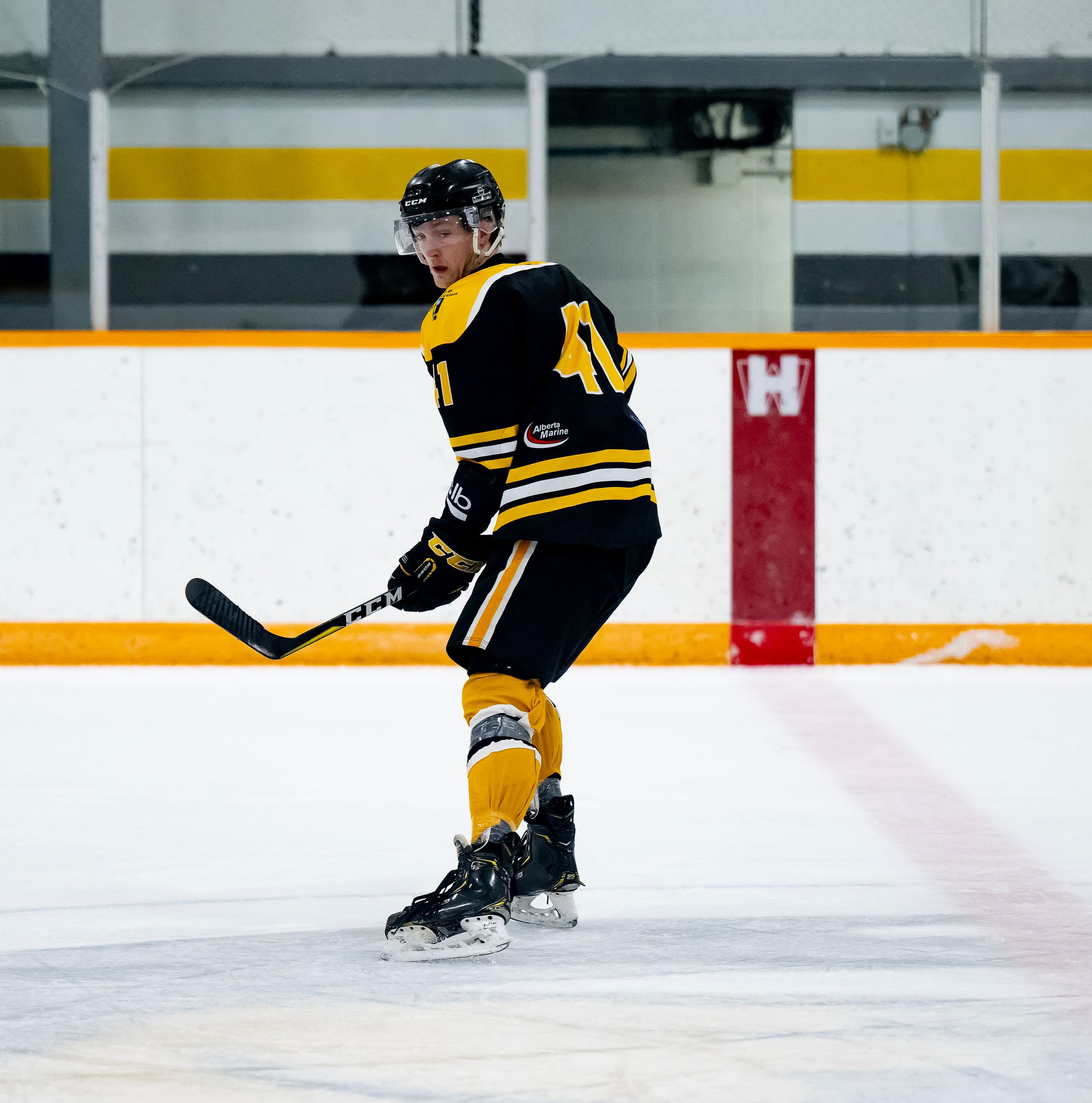 Hockey player in black and yellow uniform practices skating drills on indoor ice rink.