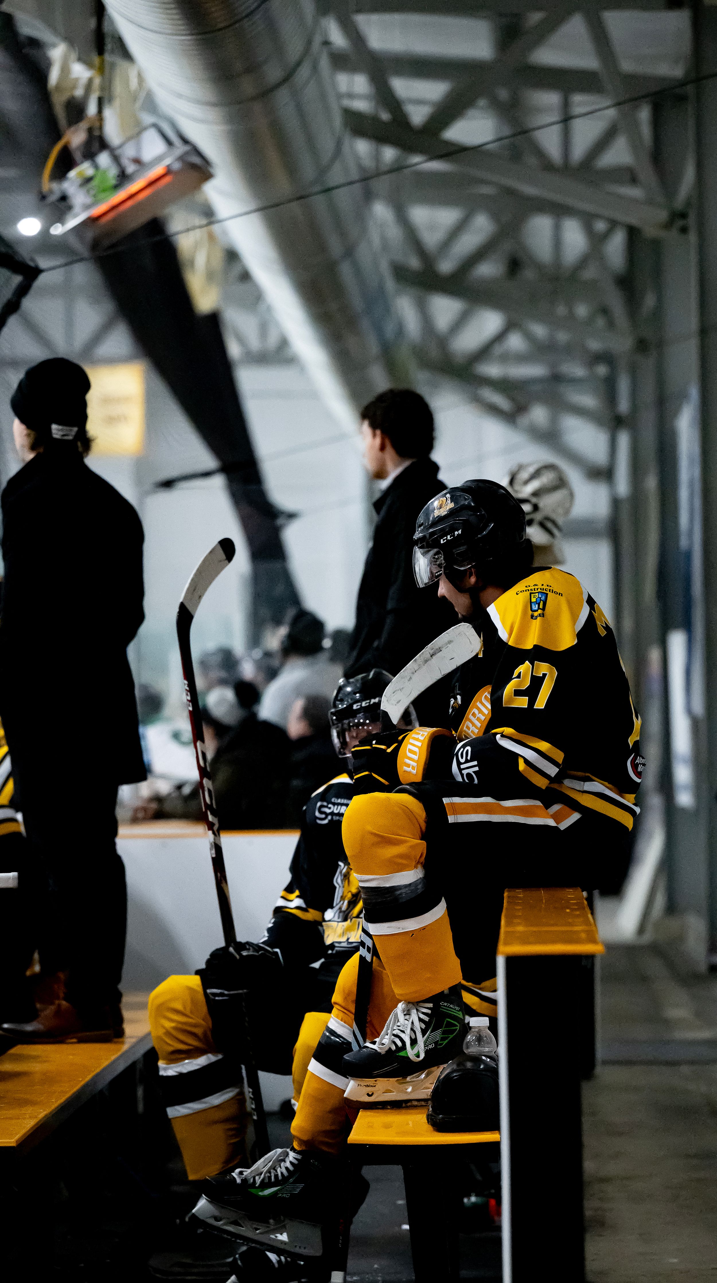 Hockey players in black and yellow uniforms sit on benches in a shadowy corridor before a game.