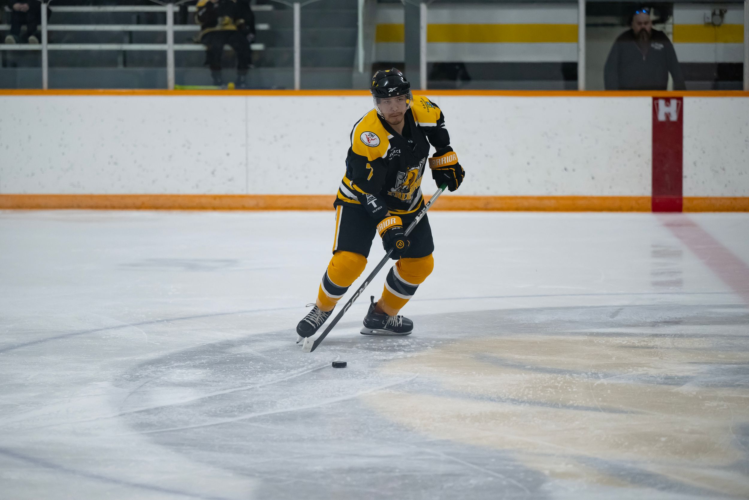 Hockey player in yellow jersey skates on ice with stick during practice session.