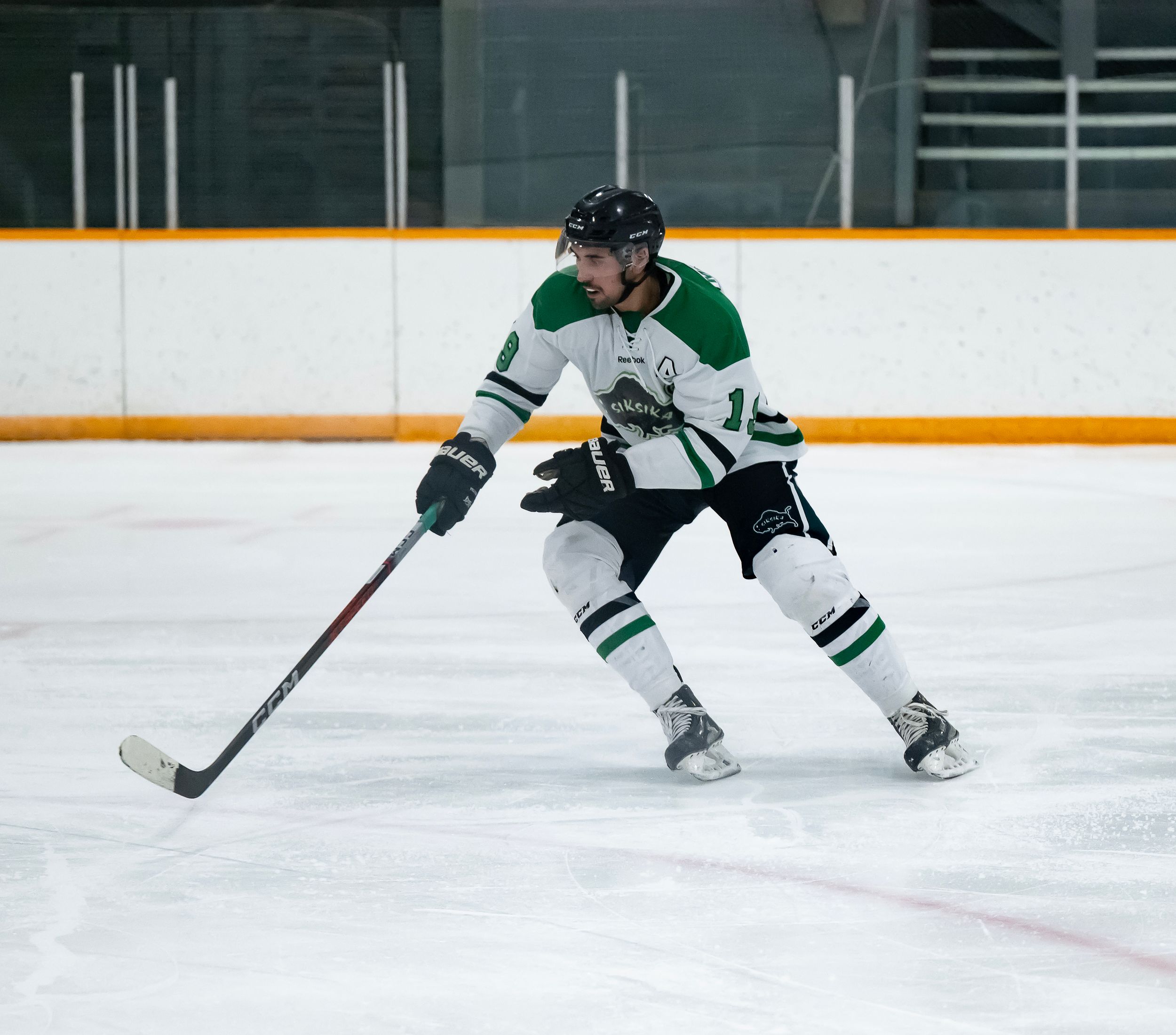 Hockey player in white jersey skates with stick on ice during competitive game action.
