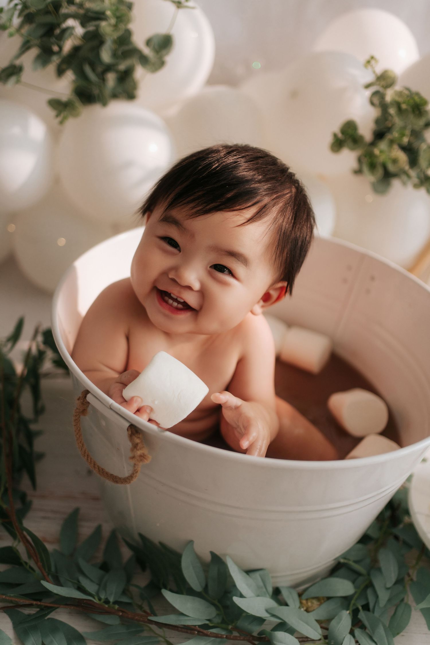 Cake smash photo session setup with white balloons, sunflowers and a baby enjoying their first birthday celebration.
