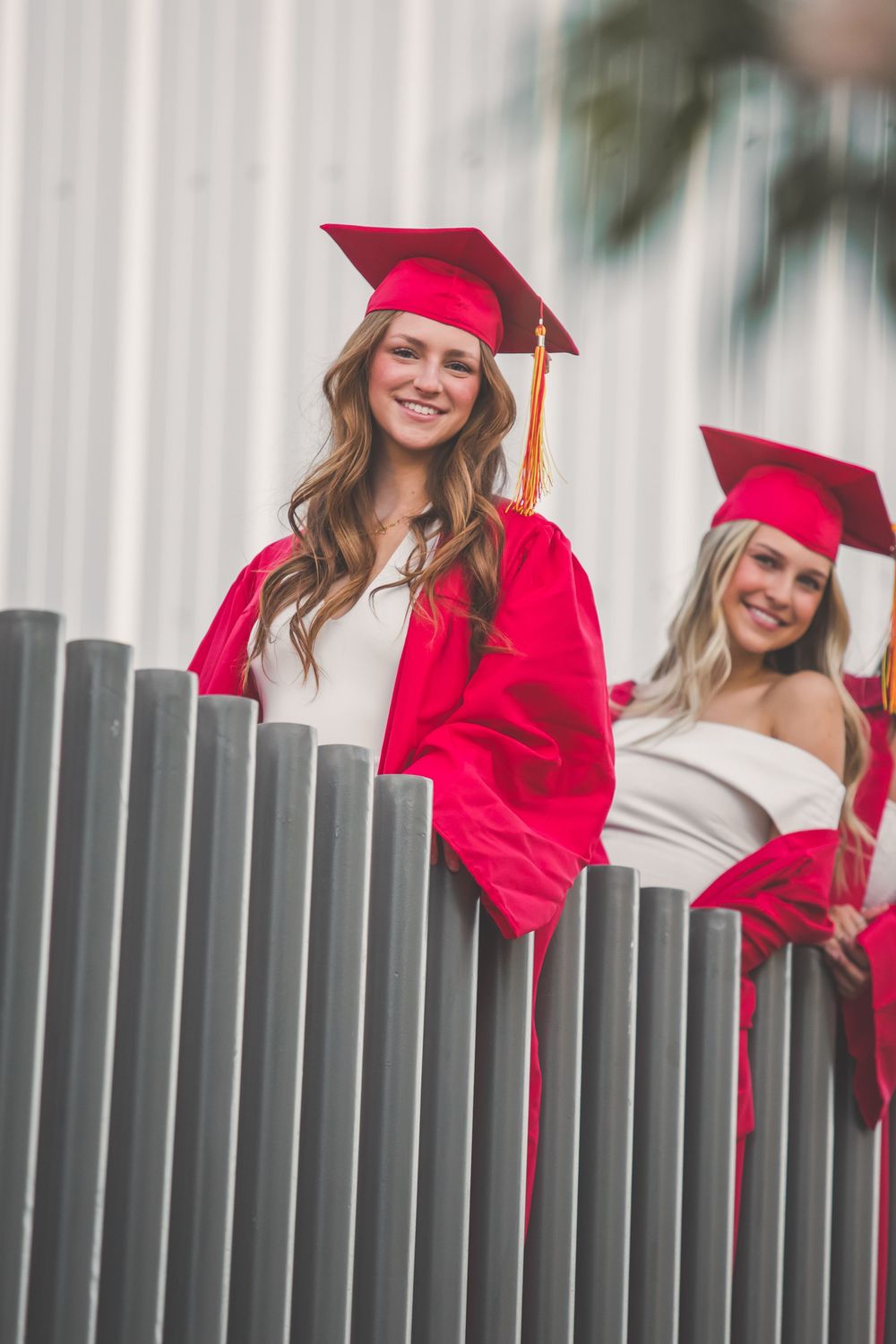 Graduates in red caps and gowns pose behind a fence during graduation photo session.