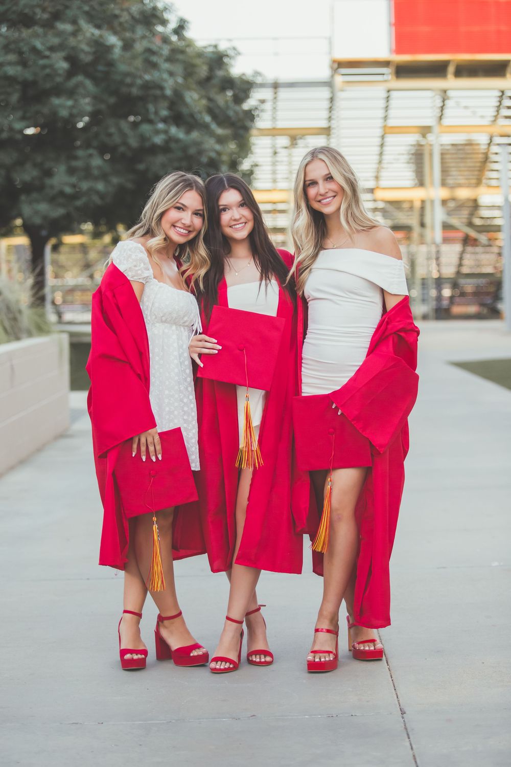 Three friends wearing red jackets and heels show off their matching outfits on a sidewalk.