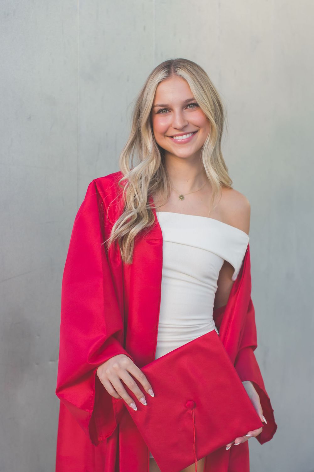 A person in a white top and vibrant red blazer poses against a gray background in a fashion photo series.