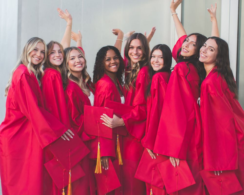 A group of people wearing bright red graduation gowns and gold tassels pose together in celebration.