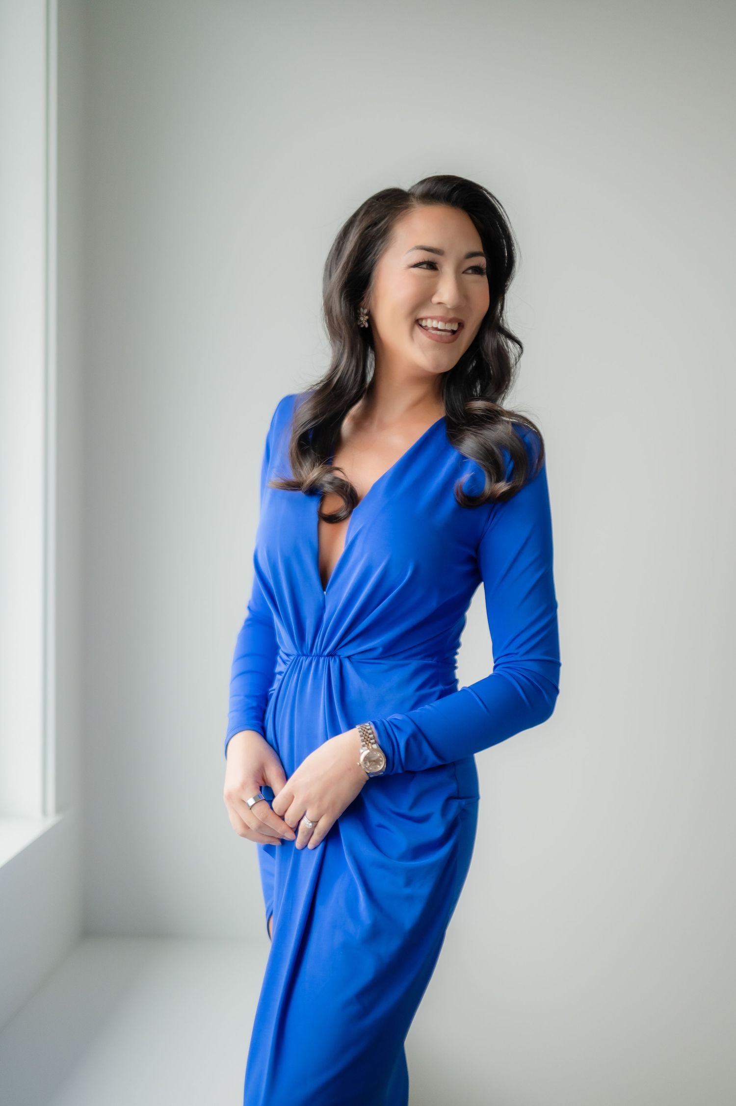 A woman poses in a vibrant royal blue wrap dress against a white wall in a series of fashion photos.