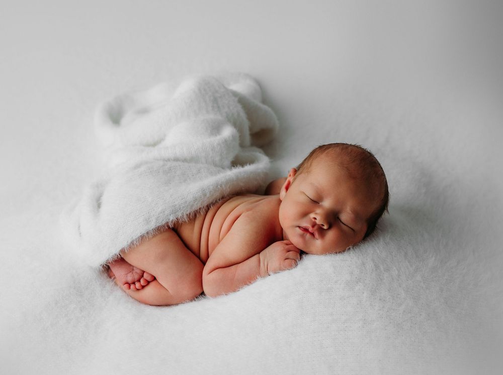 Peaceful sleeping newborn baby lying on soft white blanket during professional portrait session.