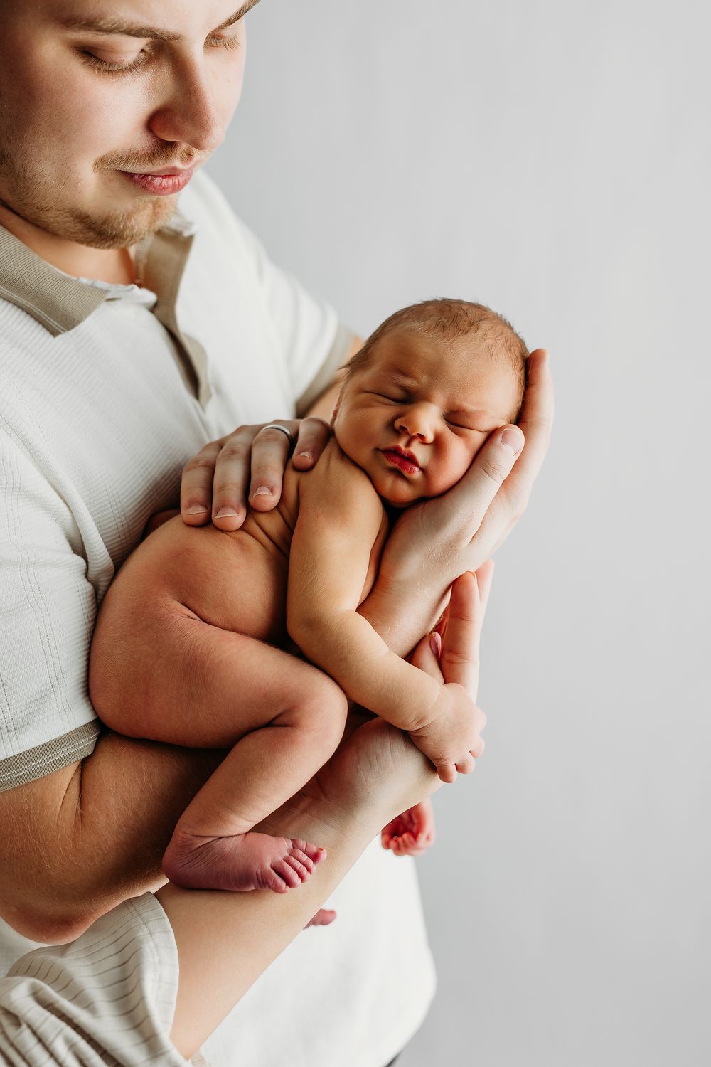 A sleeping newborn baby rests peacefully in gentle arms against a white background.