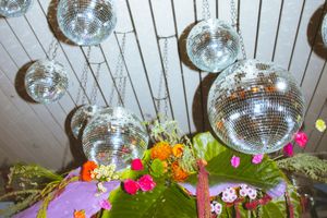 Disco balls hang above colorful floral arrangements with bright pink and orange flowers against a white ceiling.